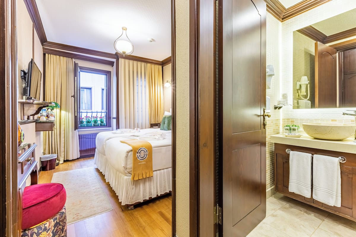 A hotel room with a bed, a bathroom with a large mirror, and a window with curtains.