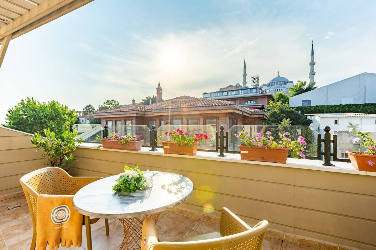 A balcony with a round table and chairs, potted plants, and a view of a mosque with a minaret.