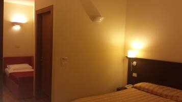 Ein Hotelzimmer mit einem Bett, einem Nachttisch, einem roten Sessel und einer Tür.
