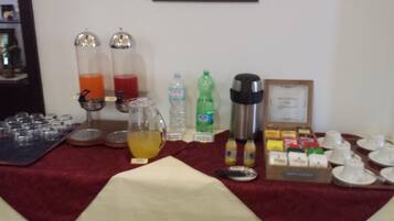 A buffet setup with various food and drink options, including a drink dispenser, bottled water, and a coffee maker.