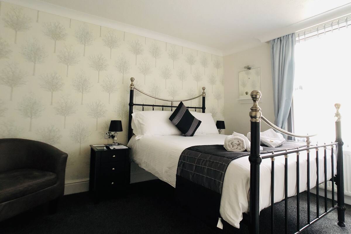 A neatly arranged bedroom with a four-poster bed, a bedside table with a lamp, and a chair.