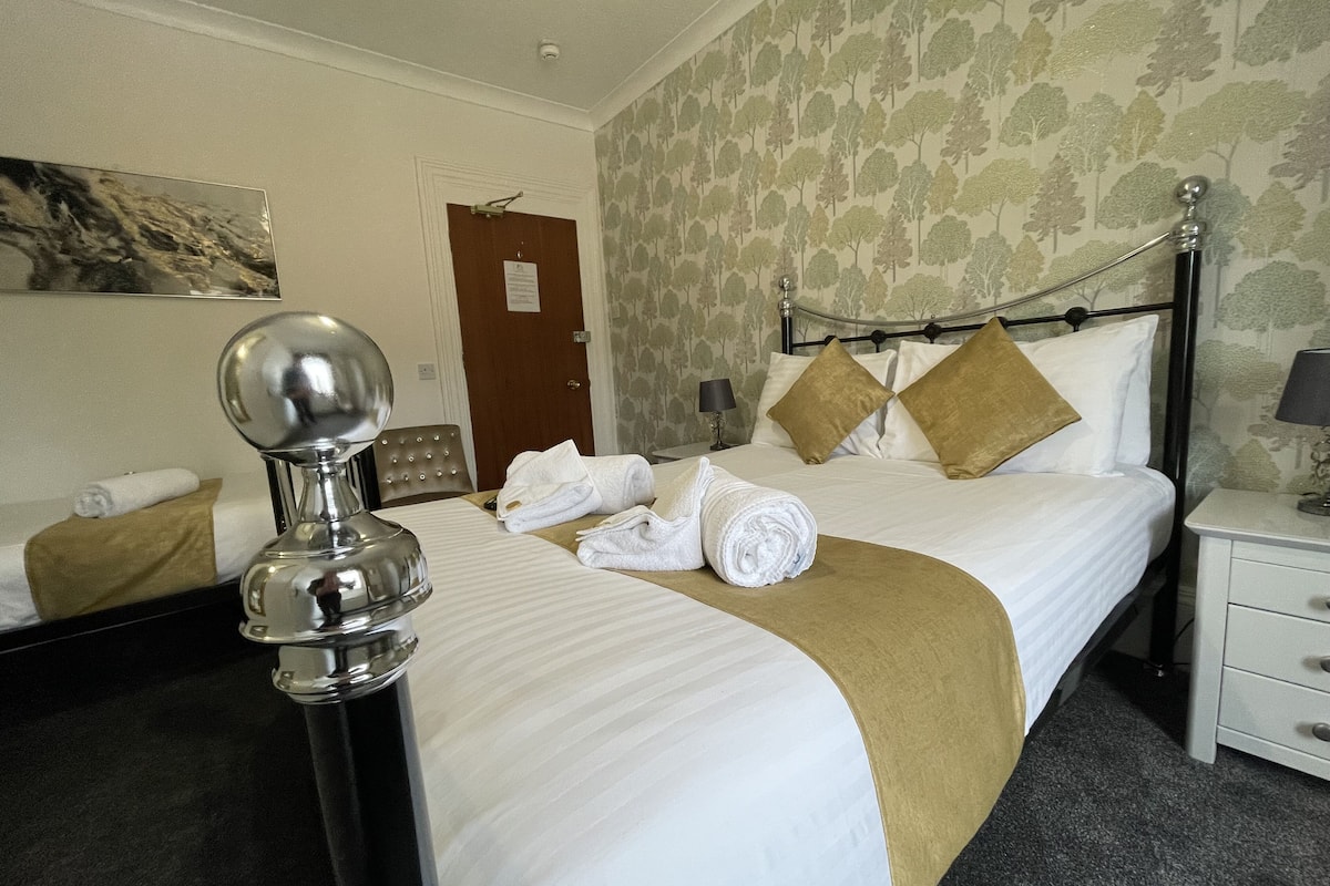 A hotel room with a neatly made bed, a bedside table with a lamp, a mirror, and a door with a sign.