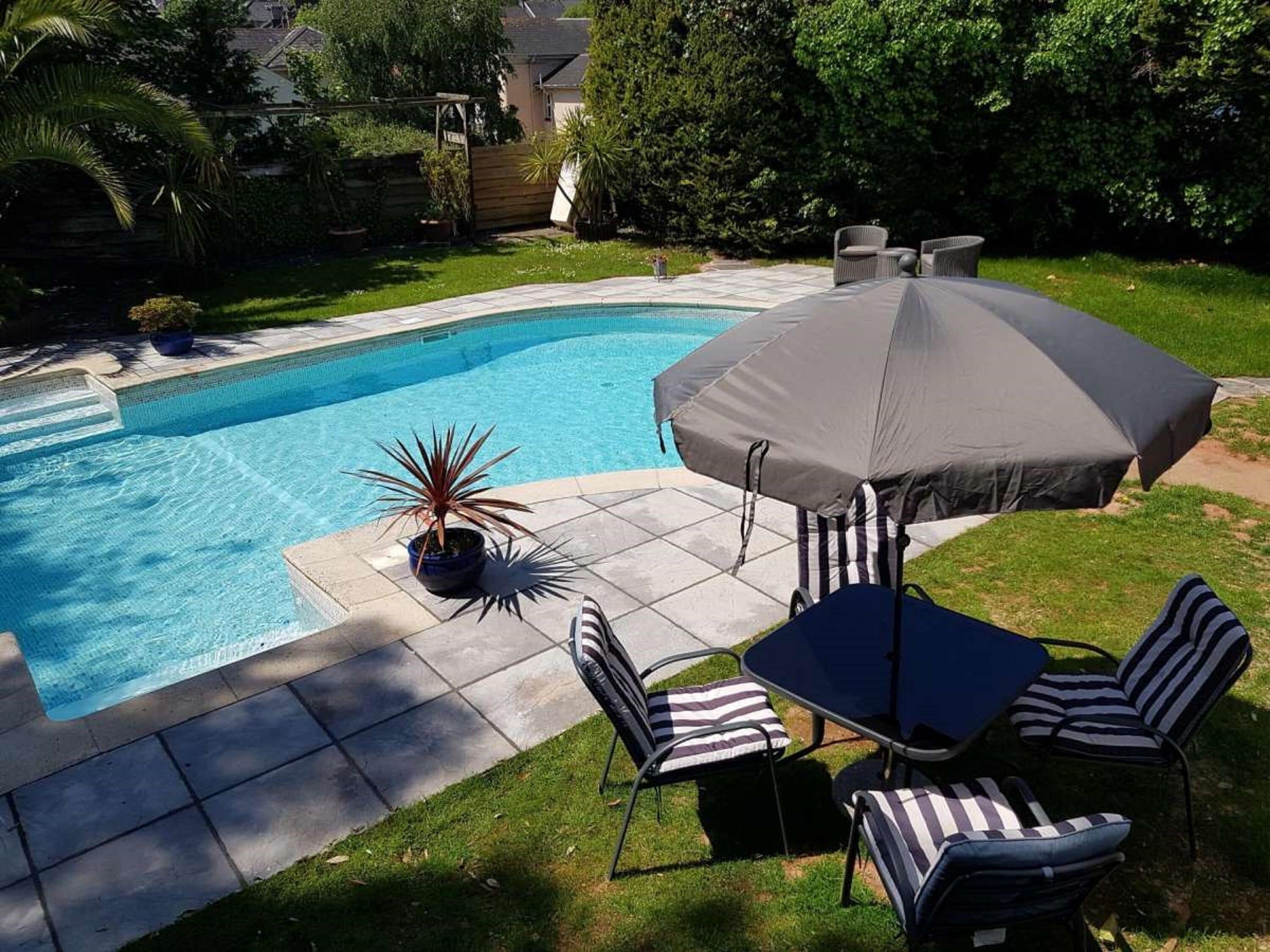 A backyard with a swimming pool, patio furniture, and a large umbrella.