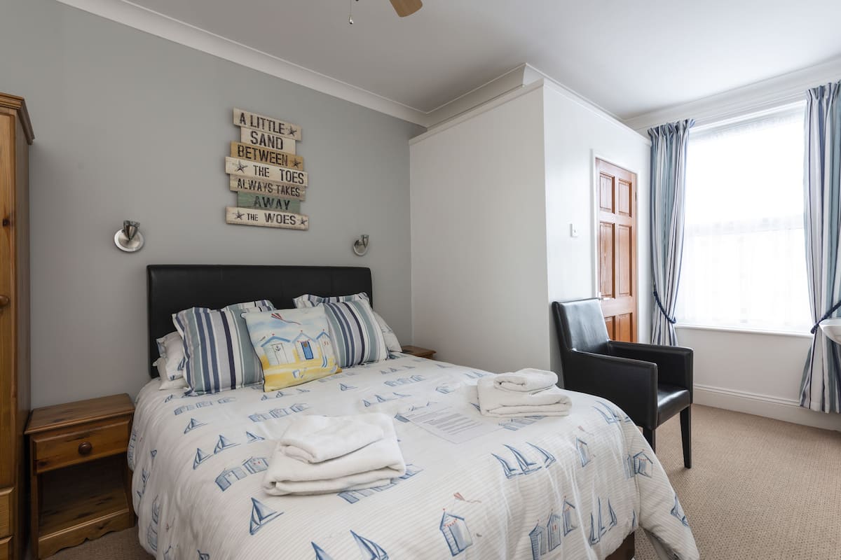 Un dormitorio ordenado con una cama, una silla y un ventanal con cortinas.
