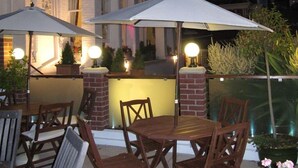 An outdoor seating area with wooden tables and chairs, two umbrellas, and potted plants. - The Shirley (Torquay)