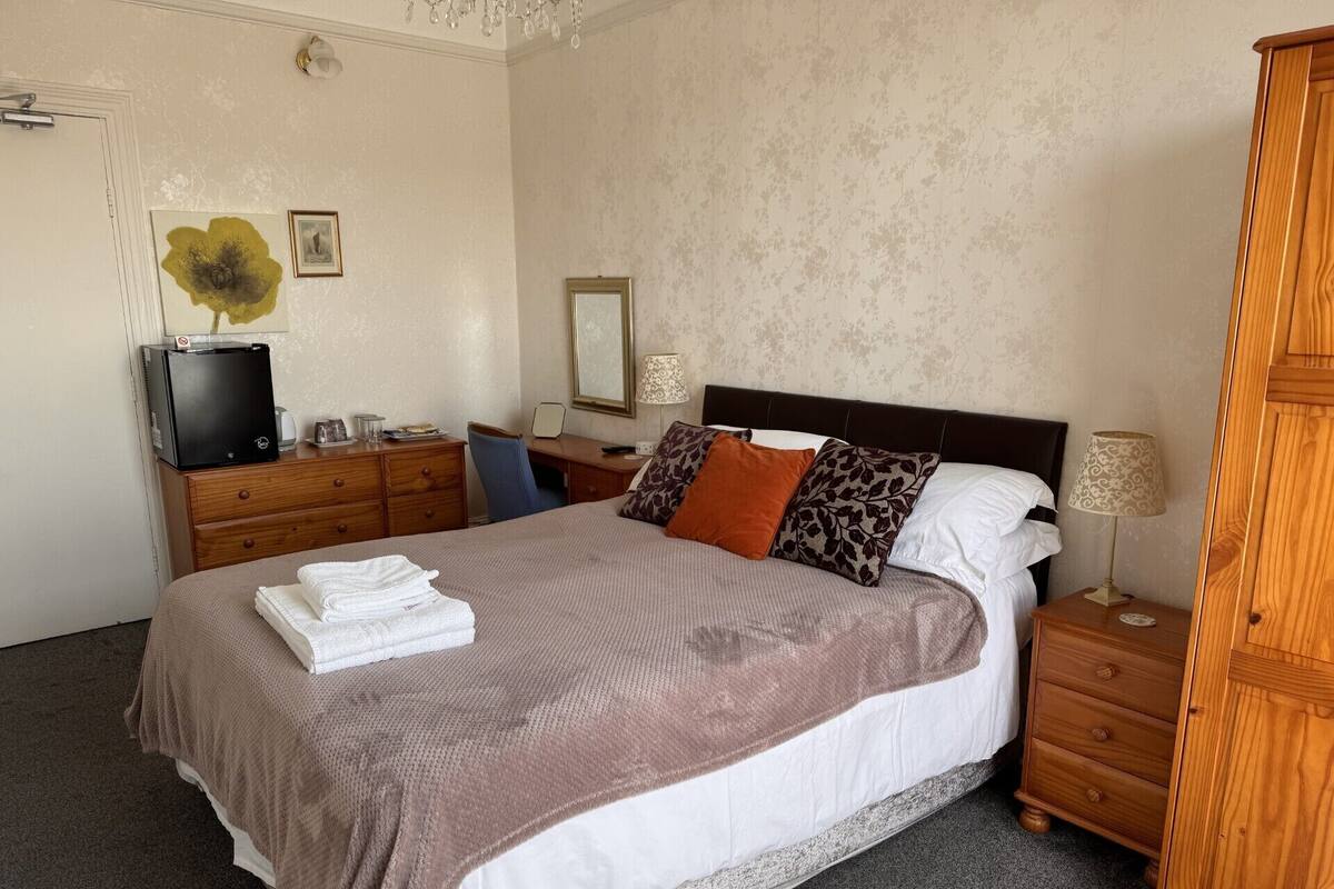 A neatly arranged bedroom with a bed, a wooden dresser, a desk, and a chair.