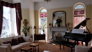 A living room with a grand piano, a sofa, a coffee table, and a fireplace. - The Shirley (Torquay)