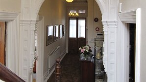 A hallway with a wooden staircase, a display cabinet with decorative items, and a door leading to another room. - The Shirley (Torquay)