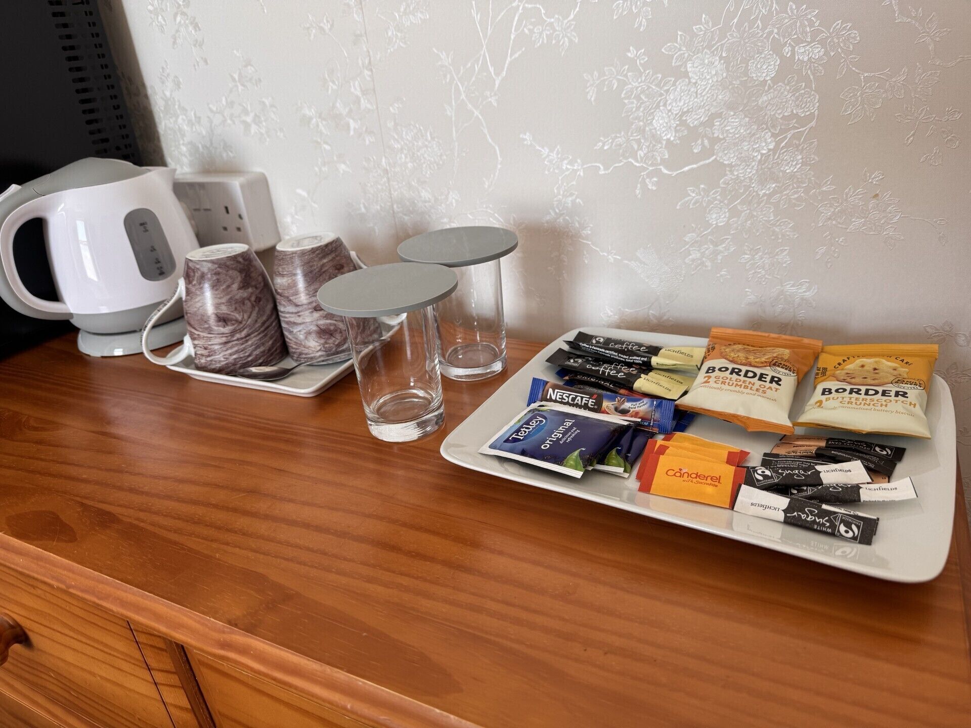 A coffee station with a white kettle, marble mugs, and a tray of coffee packets and snacks.