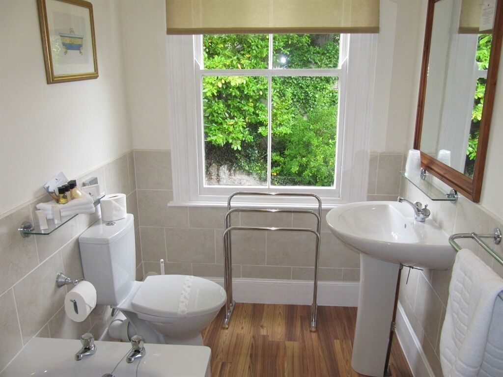 Une salle de bain comprenant des toilettes, un bidet et un lavabo, une fenêtre donnant sur un espace verdoyant et un miroir au-dessus du lavabo.