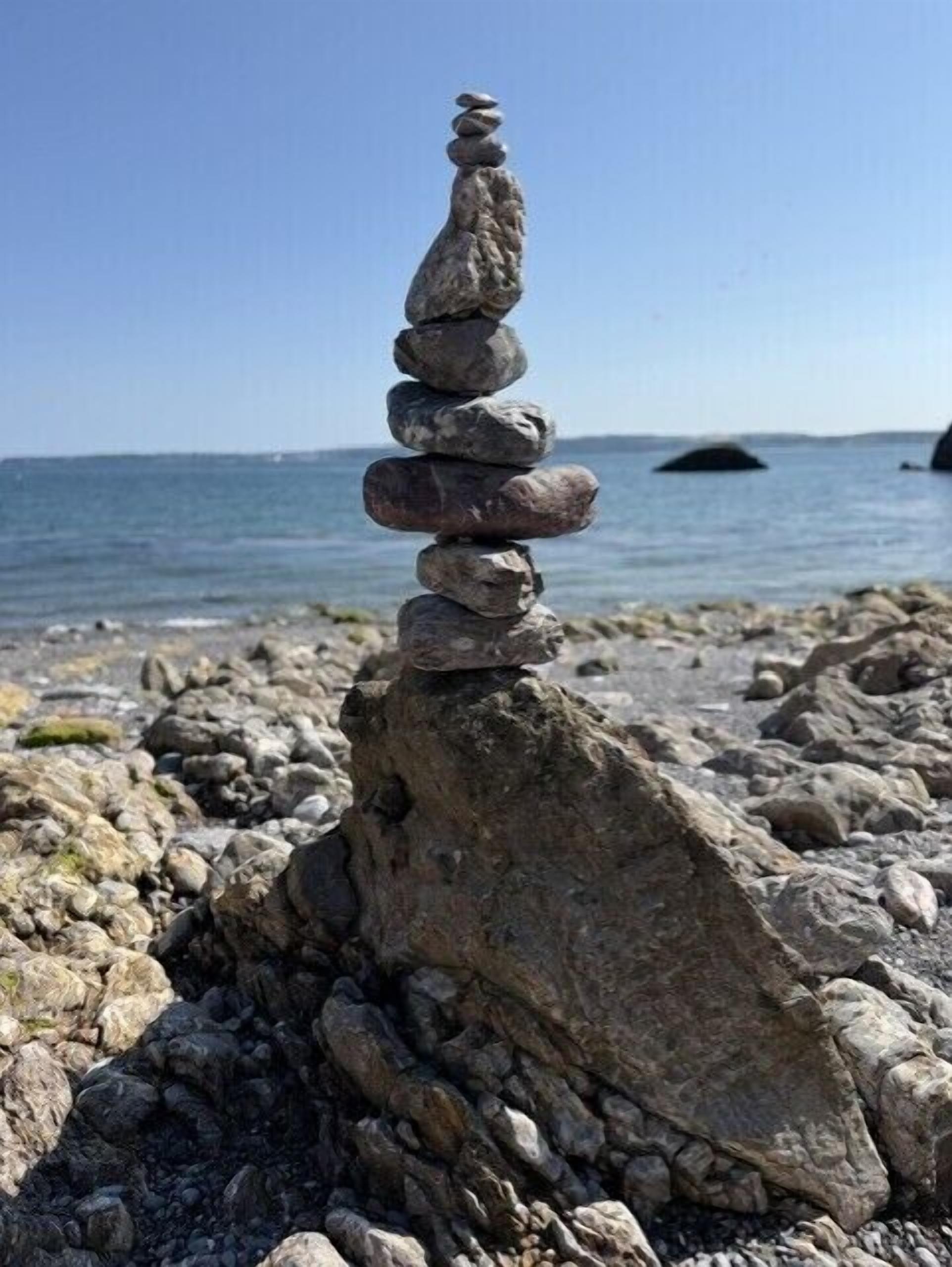 A stack of stones on a rocky beach with a view of the sea.