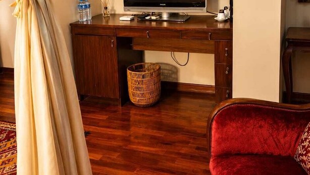 A living room with a wooden floor, a red sofa, a television on a wooden stand, a framed picture on the wall, and a basket on the floor. - Villa Sphendone Suites (Istanbul)