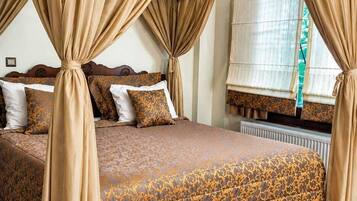 A four-poster canopy bed with a patterned bedspread, a wooden floor, and a window with curtains.