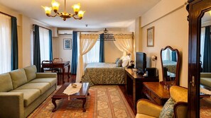 A hotel room with a bed, sofa, desk, television, and a mirror. - Villa Sphendone Suites (Istanbul)
