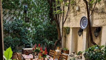 An outdoor patio with a wooden table and chairs, surrounded by potted plants and a stone wall.