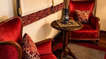A room with two red velvet armchairs, a small round table with a vase, and a patterned rug.