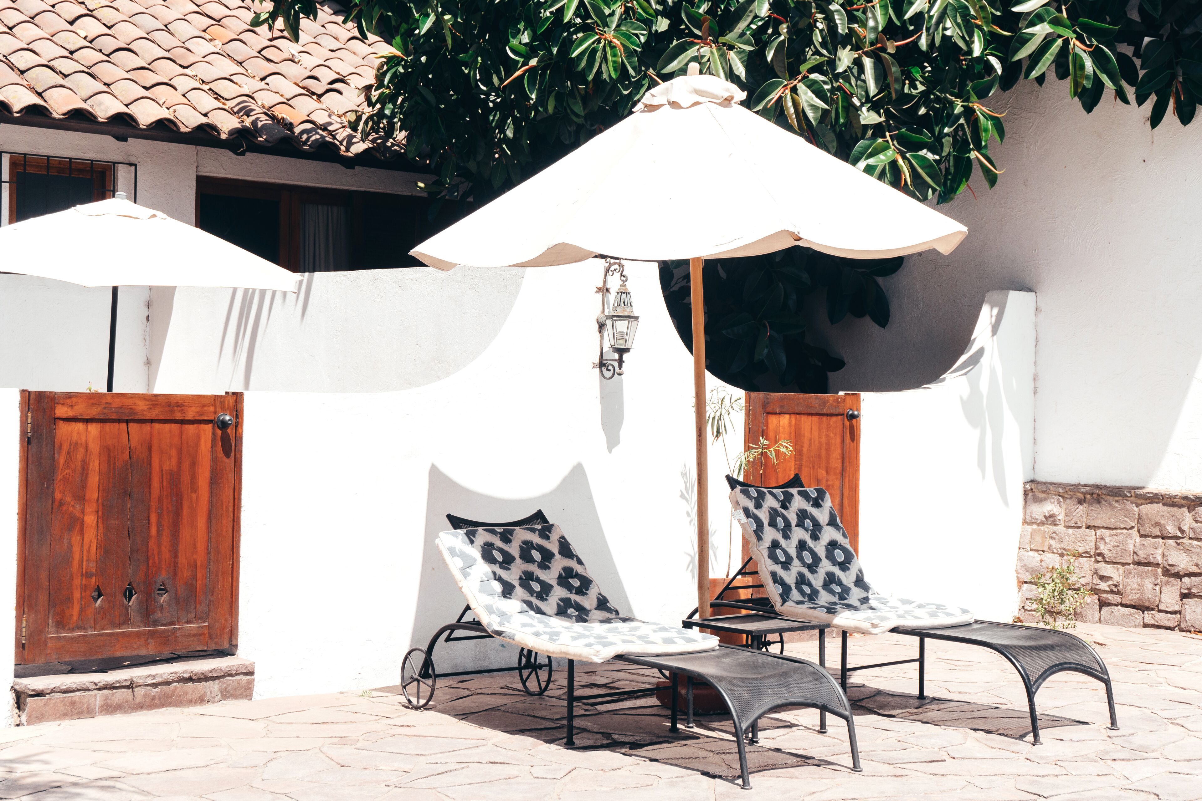 Dos sillones de relax con cojines estampados, una puerta de madera y una pared blanca con techo de tejas.