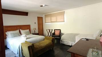 Un dormitorio con una cama grande, una cama más pequeña, una silla, una mesa y una ventana con persianas.