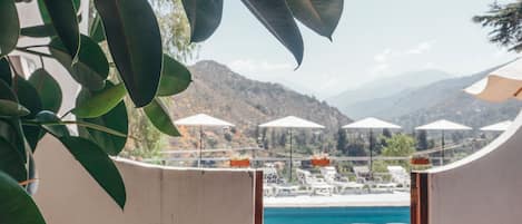 A view of a pool area with lounge chairs and umbrellas, surrounded by greenery and mountains in the background.