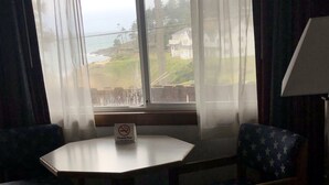 A hotel room with a round table, two armchairs, a view of the sea, and a 'No Smoking' sign.