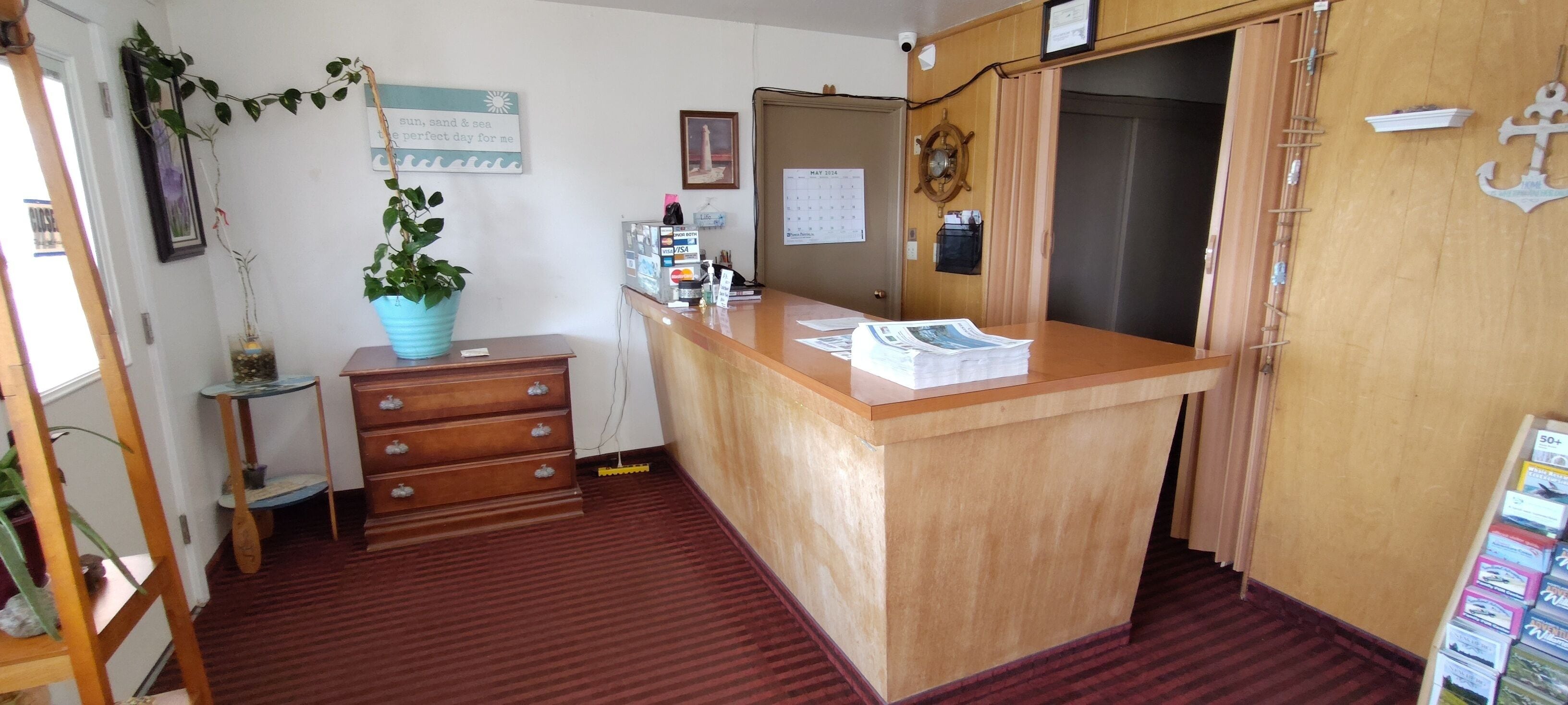 A reception area with a wooden desk, a potted plant, a calendar, and a wall-mounted coat rack.