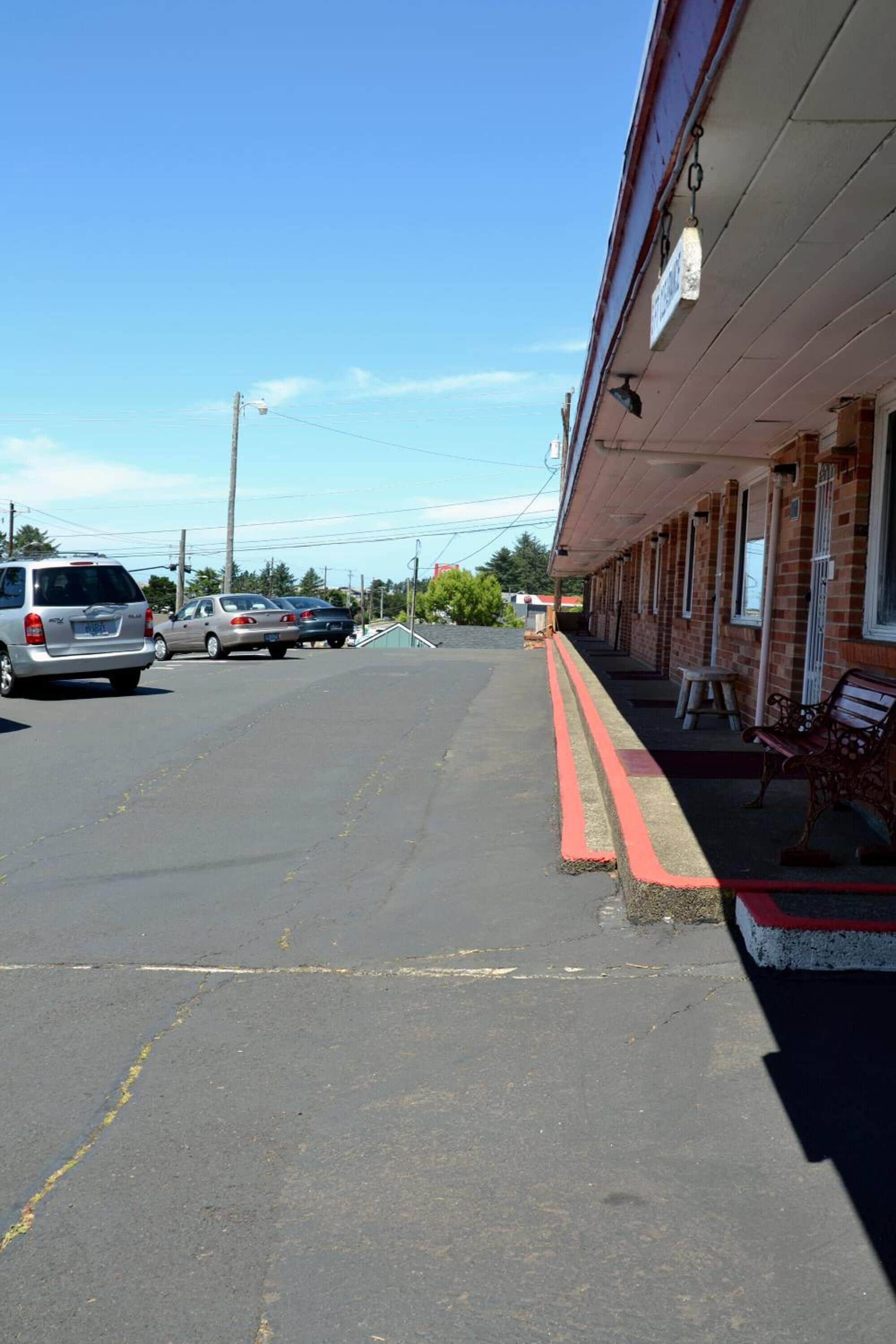 A street with a building on the right. There are cars parked on the street.