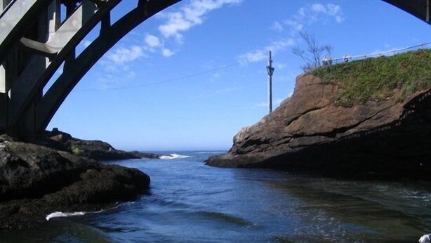 A bridge over a body of water with rocky terrain on one side and a clear sky.