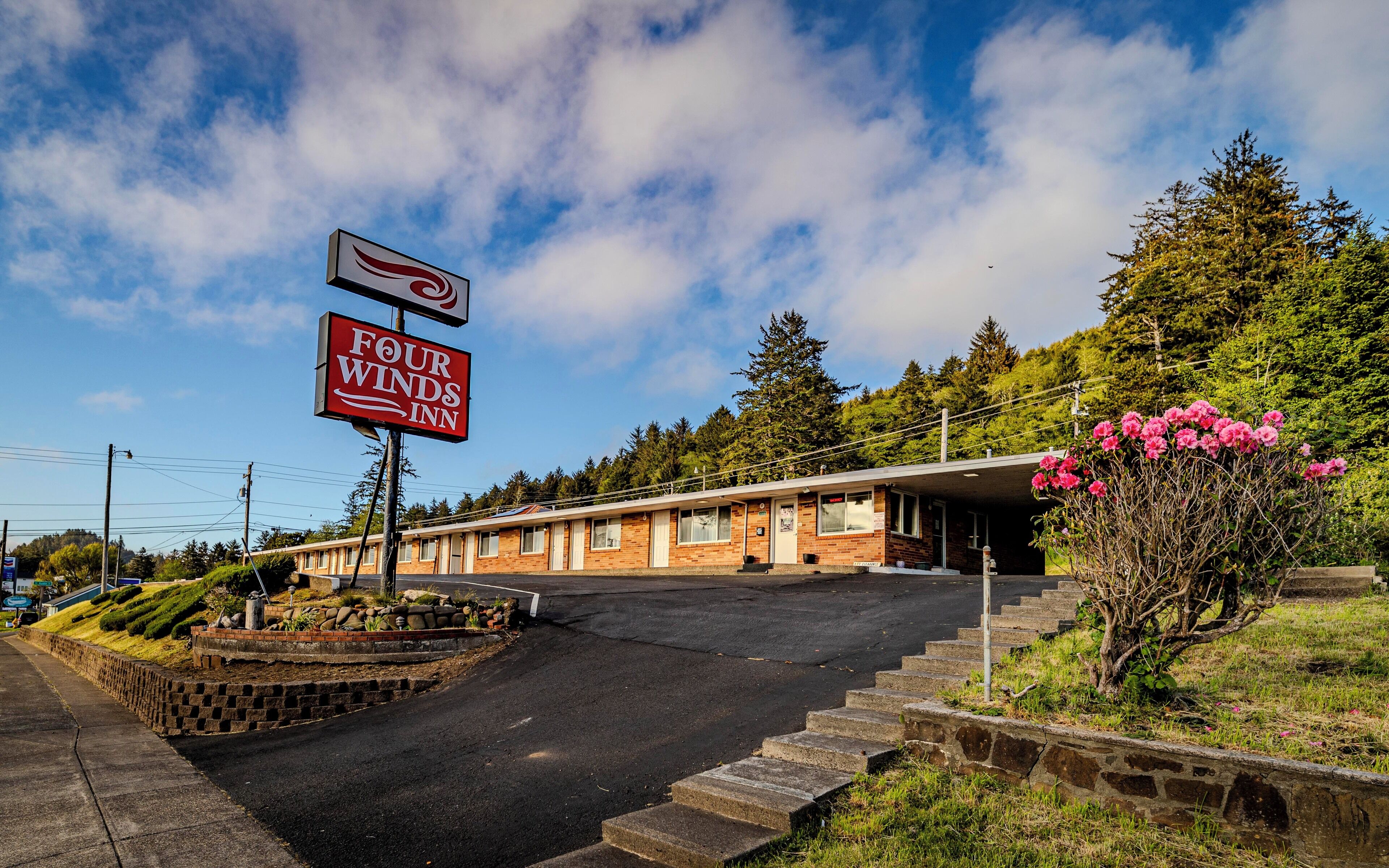 A Four Winds Inn with a brick building, a parking lot, and a staircase leading to the entrance.