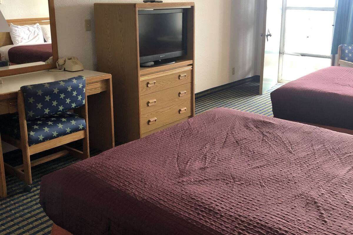 Quarto de hotel com duas camas, uma escrivaninha com cadeira, televisão e um espelho grande.