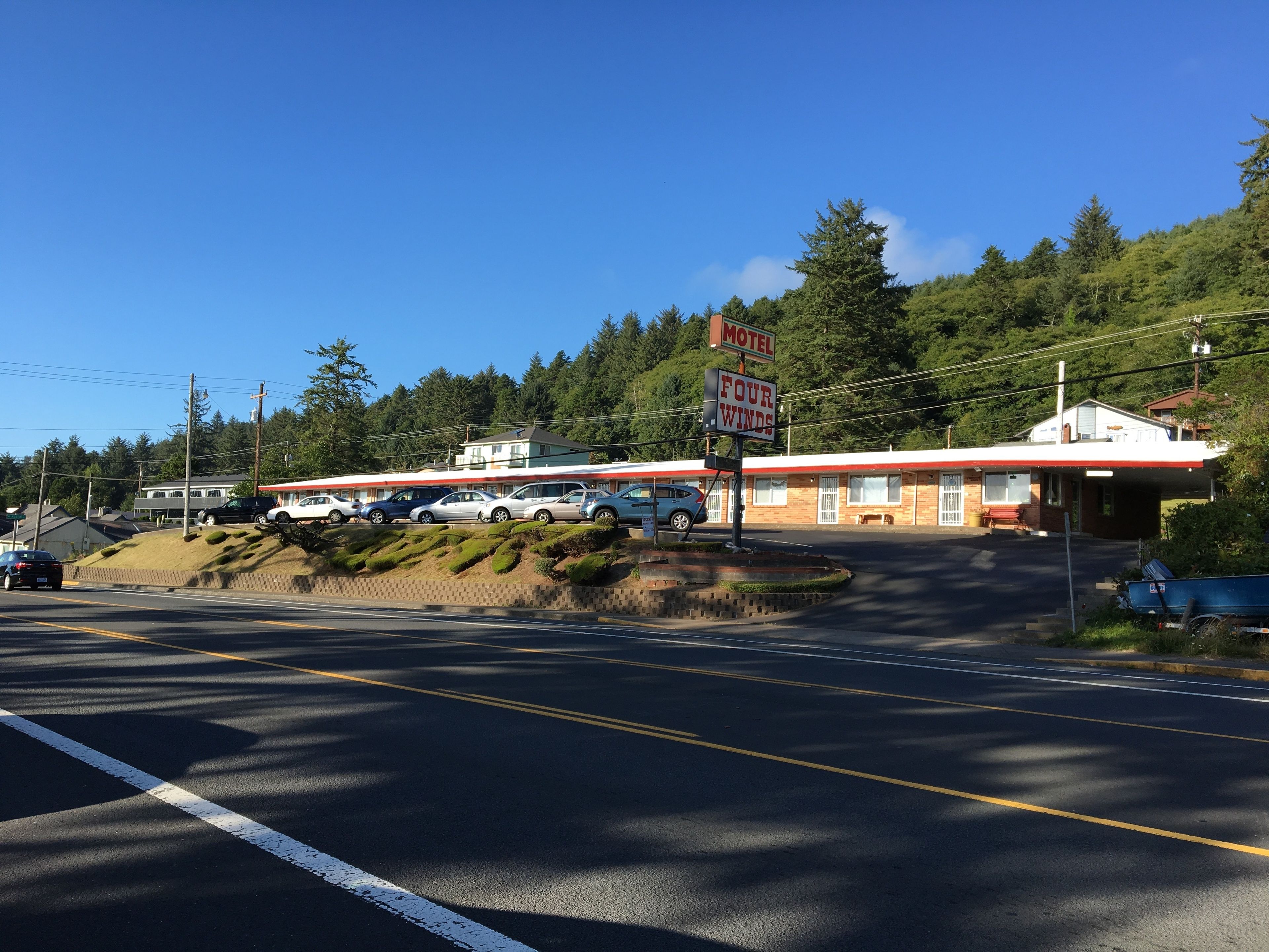 A motel with a red and white exterior, a parking lot with several cars, and a mountainous backdrop.