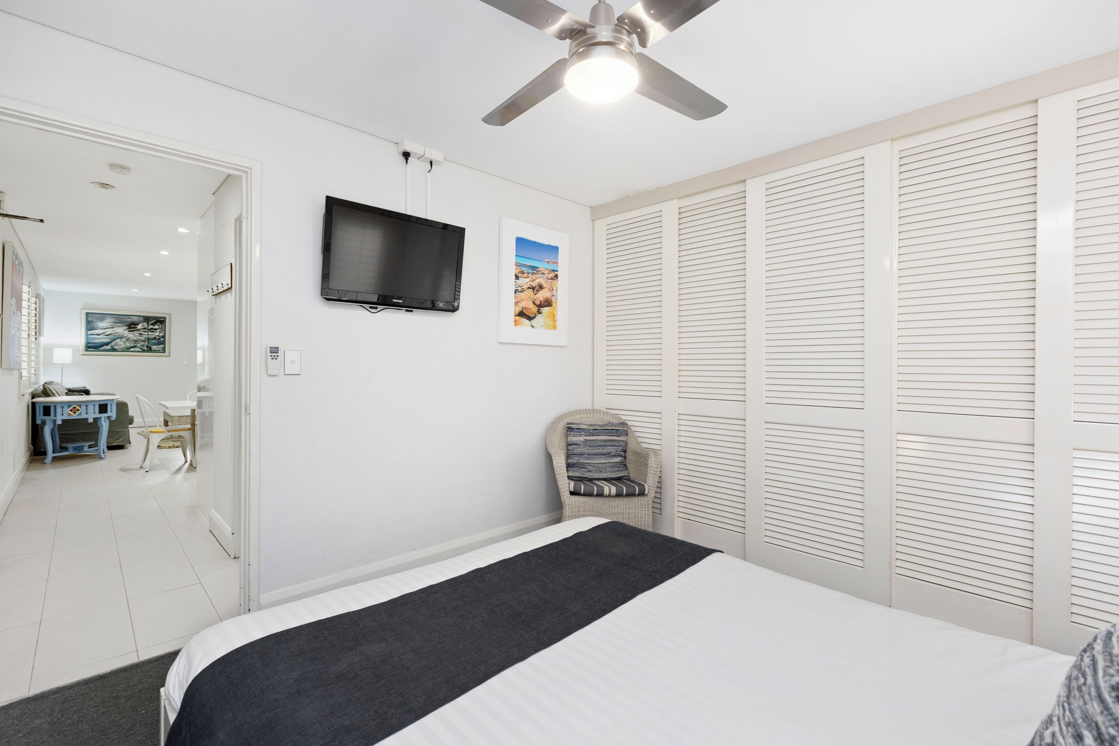 Un dormitorio con cama, ventilador de techo, televisor y armario con puertas empañadas.