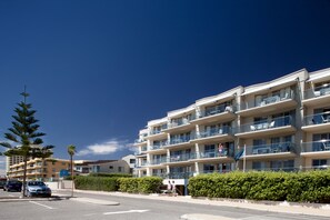 A multi-story hotel with balconies, a parking area, and a clear blue sky.