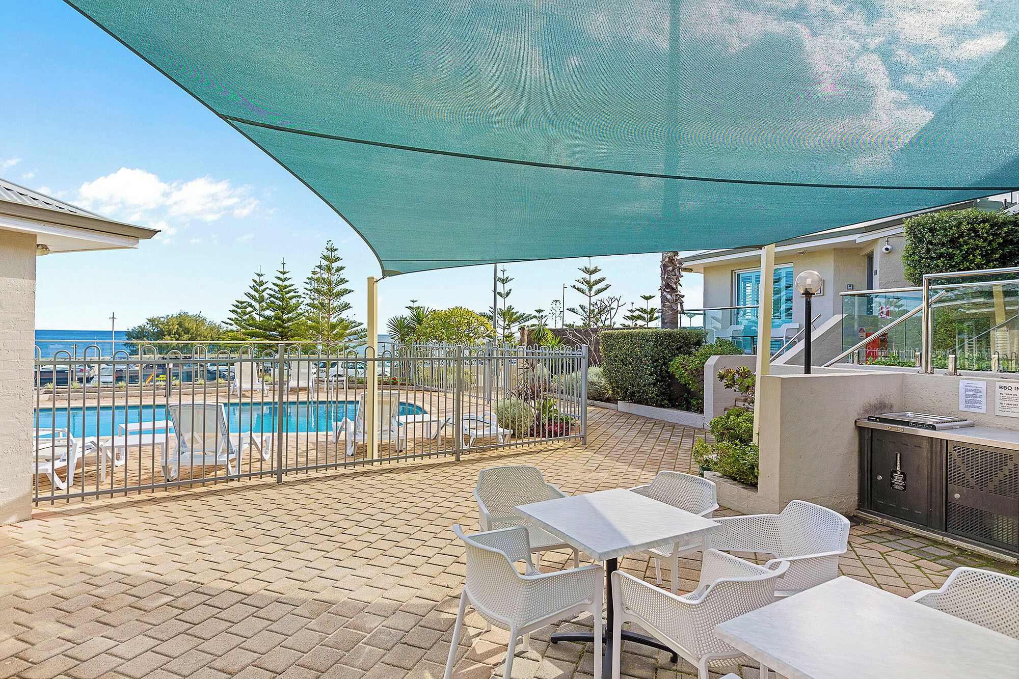 A poolside area with a covered seating area, a pool, and a view of the ocean.