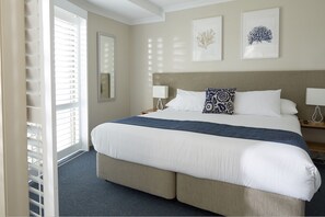 A hotel room with a large bed, two bedside tables, and a window with blinds.