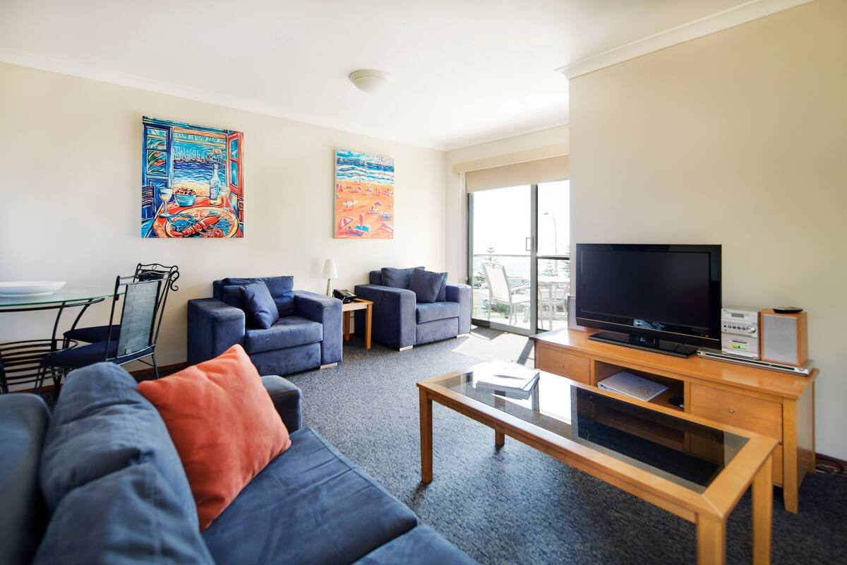 A modern living room with a sofa, armchairs, a coffee table, a TV, and artwork on the walls.