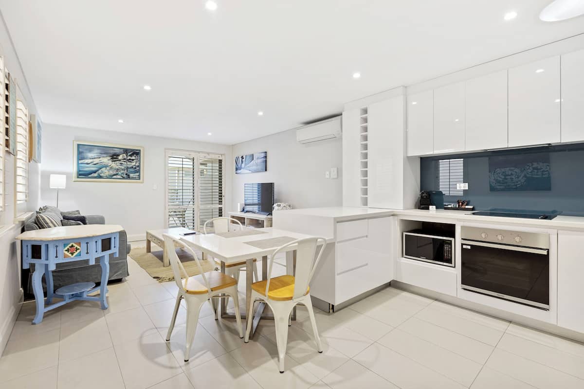 A modern kitchen with white cabinetry, a dining area with a white table and chairs, and a TV mounted on the wall.