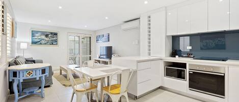 A modern kitchen with white cabinetry, a dining area with a white table and chairs, and a TV mounted on the wall.