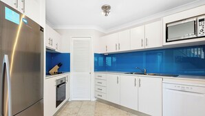 A modern kitchen with white cabinets, stainless steel appliances, a blue backsplash, and a tiled floor. - Seashells Scarborough (Scarborough)