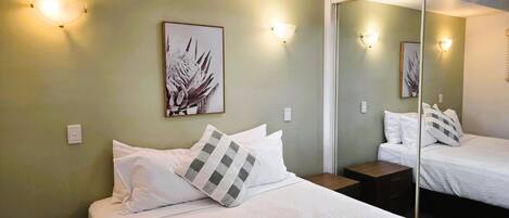 Una habitación de hotel con una cama, una mesita de noche, un espejo e iluminación en la pared.