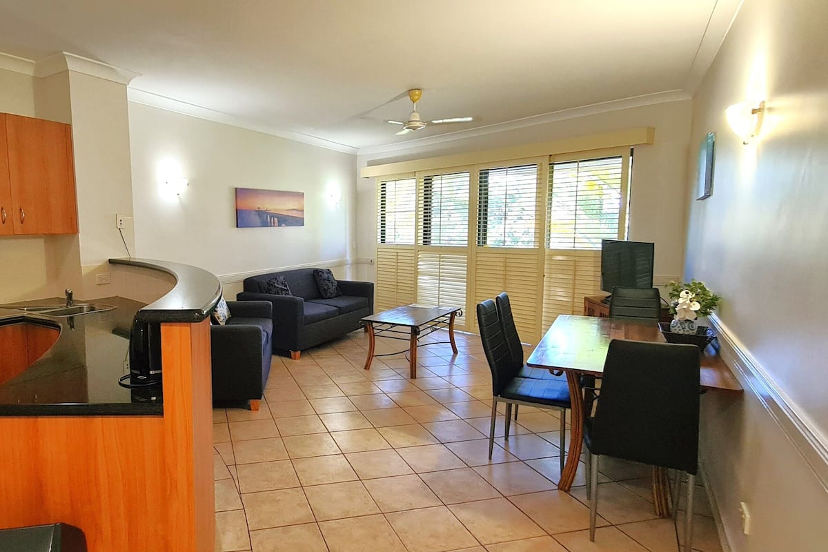 A compact kitchen with wooden cabinets, a dining area with a table and chairs, and a sofa.