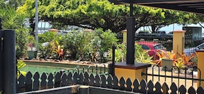 Un espacio exterior cercado con piscina, rodeado de vegetación y un edificio amarillo.