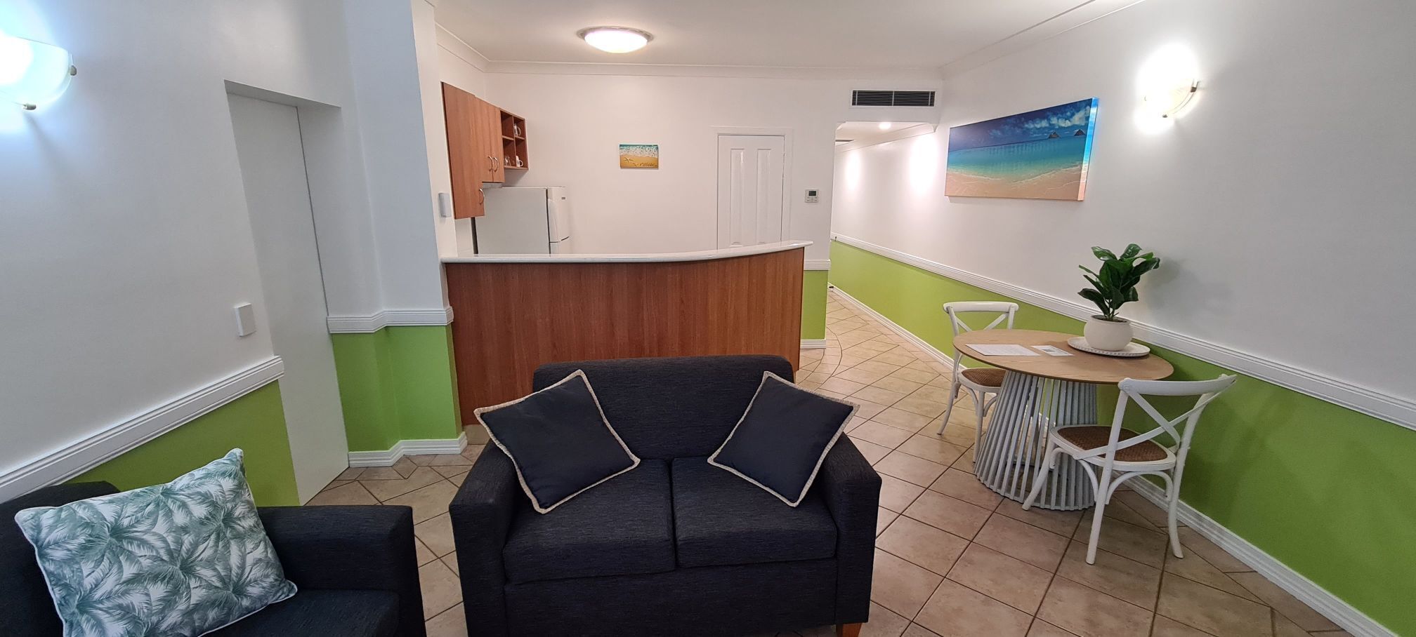 A living room with a sofa and chairs, a kitchen area with cabinets, a dining table with chairs, and a painting on the wall.