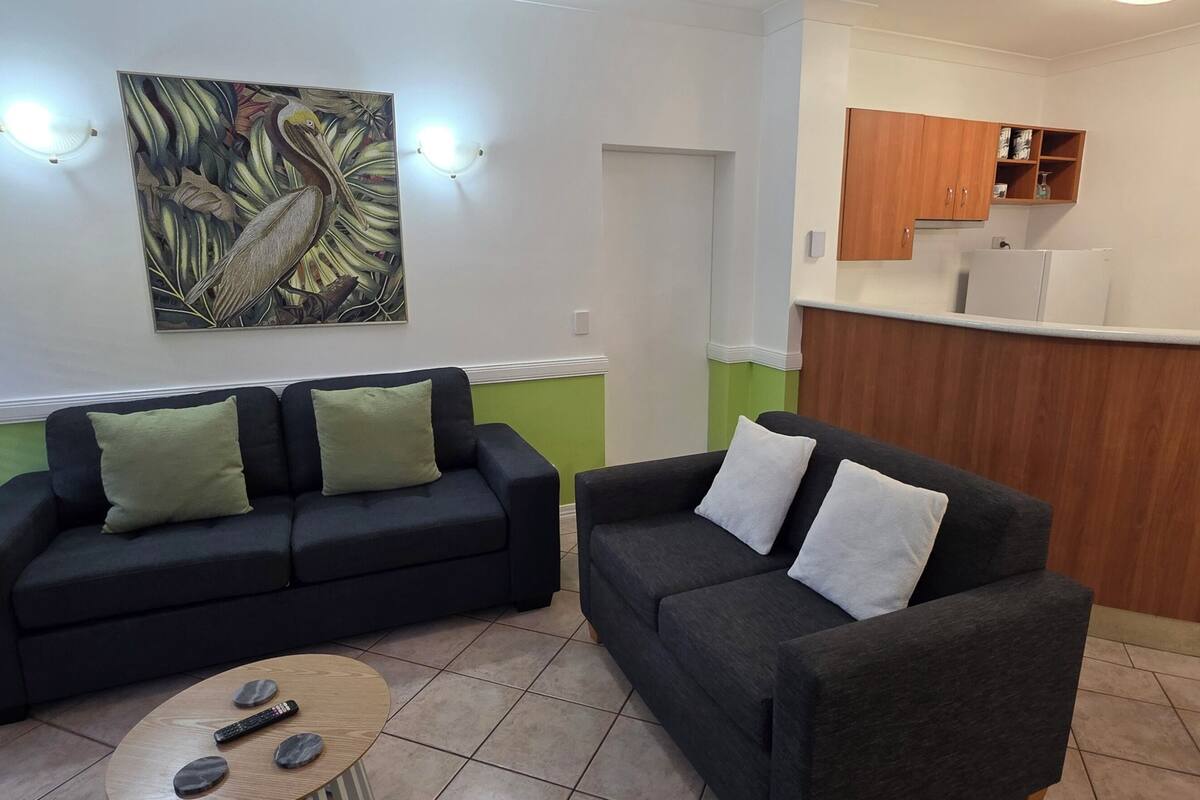 A living room with two sofas, a coffee table, and a kitchen area with wooden cabinets and a refrigerator.