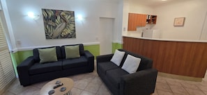 Sala de estar con dos sofás, una mesa de centro y una cocina con armarios de madera y un refrigerador.