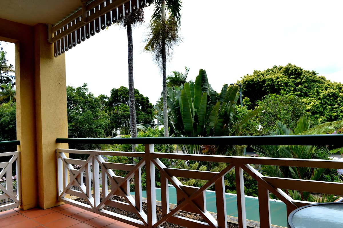 A balcony with a white railing, overlooking a lush garden with various trees and plants.