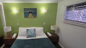 A hotel room with a bed, two bedside tables with lamps, a painting on the wall, and a window with blinds. - Waterfront Terraces (Cairns North)