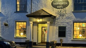 A traditional building with a sign reading "The Thorverton Arms." It features a central entrance with a small porch, multiple windows, and a paved front area. - Thorverton Arms (Exeter)
