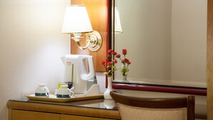 Une chambre d’hôtel avec un bureau en bois, une machine à café, une lampe et un vase rempli de fleurs.