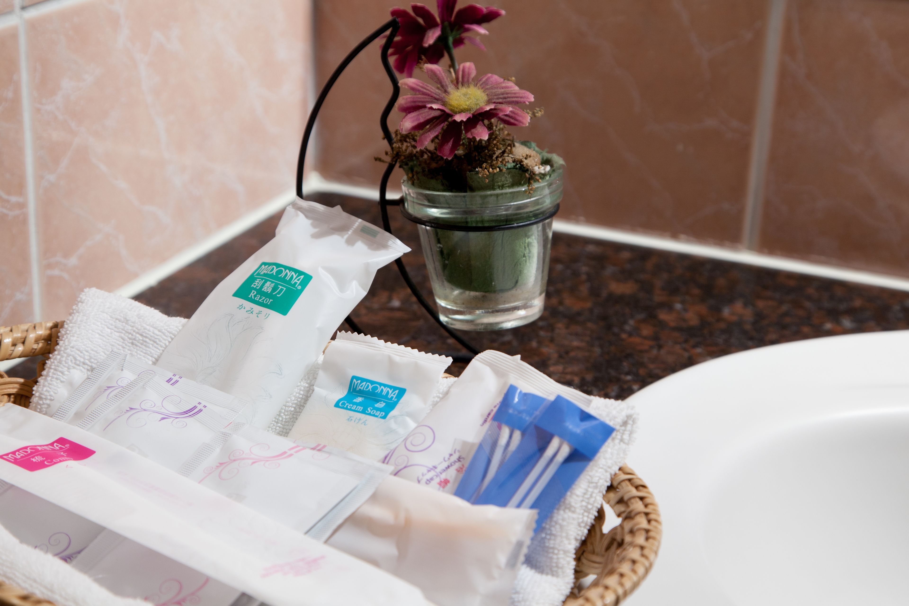 A bathroom with a marble-tiled wall, a glass jar with a flower, and a basket containing toiletries.