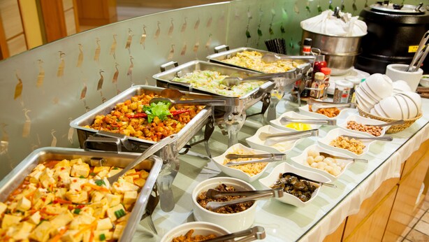 Un buffet proposant une variété d’aliments présentés dans des plateaux et des bols, notamment du tofu, des légumes et d’autres plats.